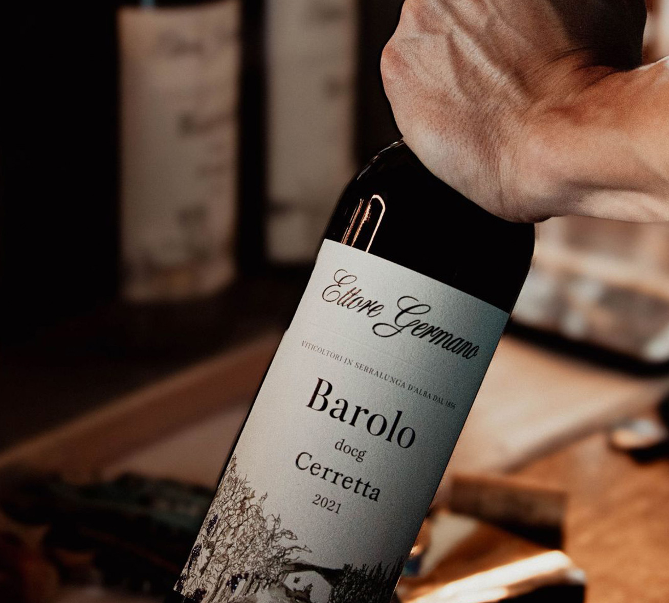 bottiglia di barolo cerretta ettore germano aperta a mano durante una visita in cantina, dettaglio dell’etichetta e del gesto di servizio